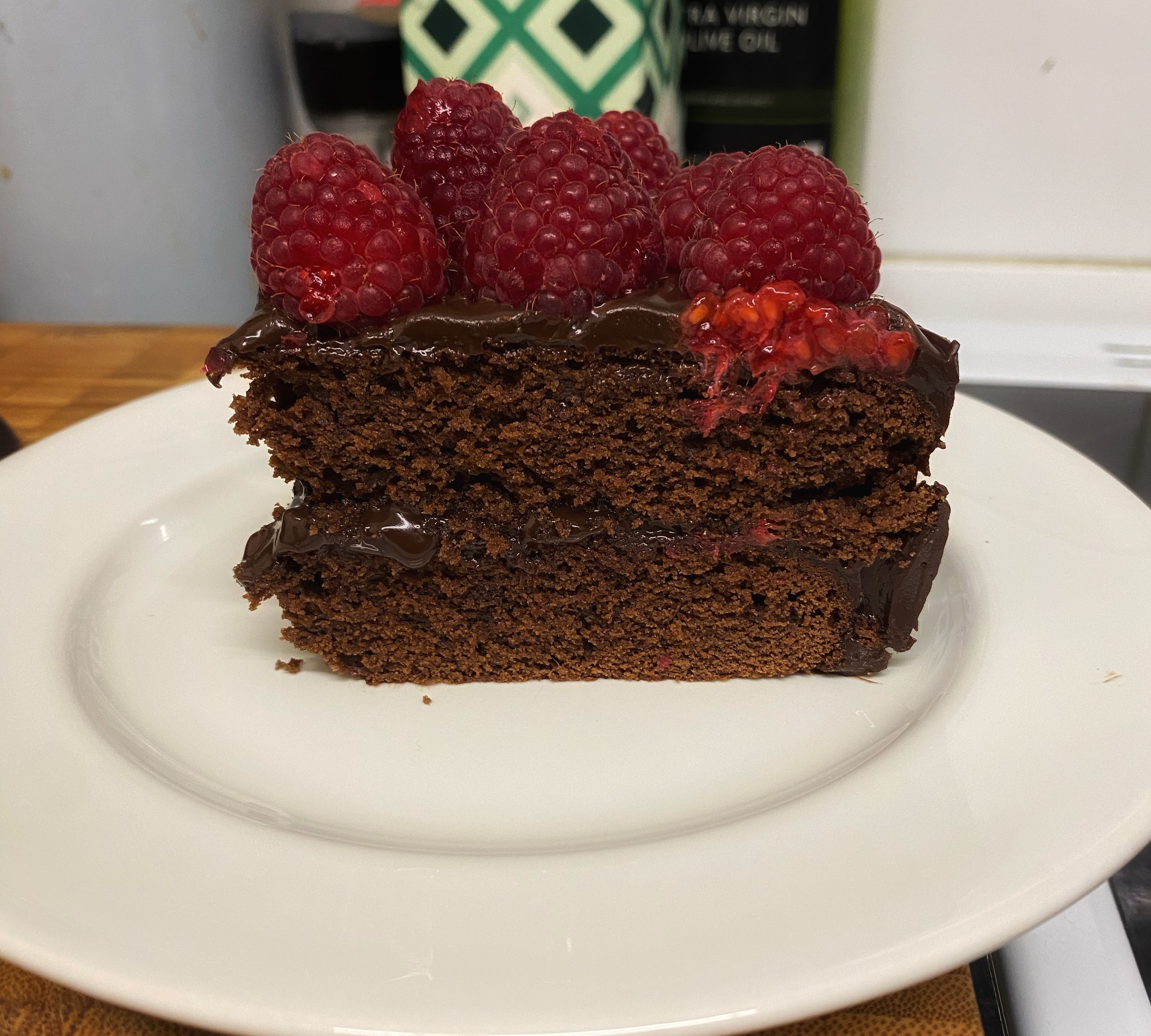 A single slice of chocolate cake, topped with raspberries. One of the raspberries is smushed.