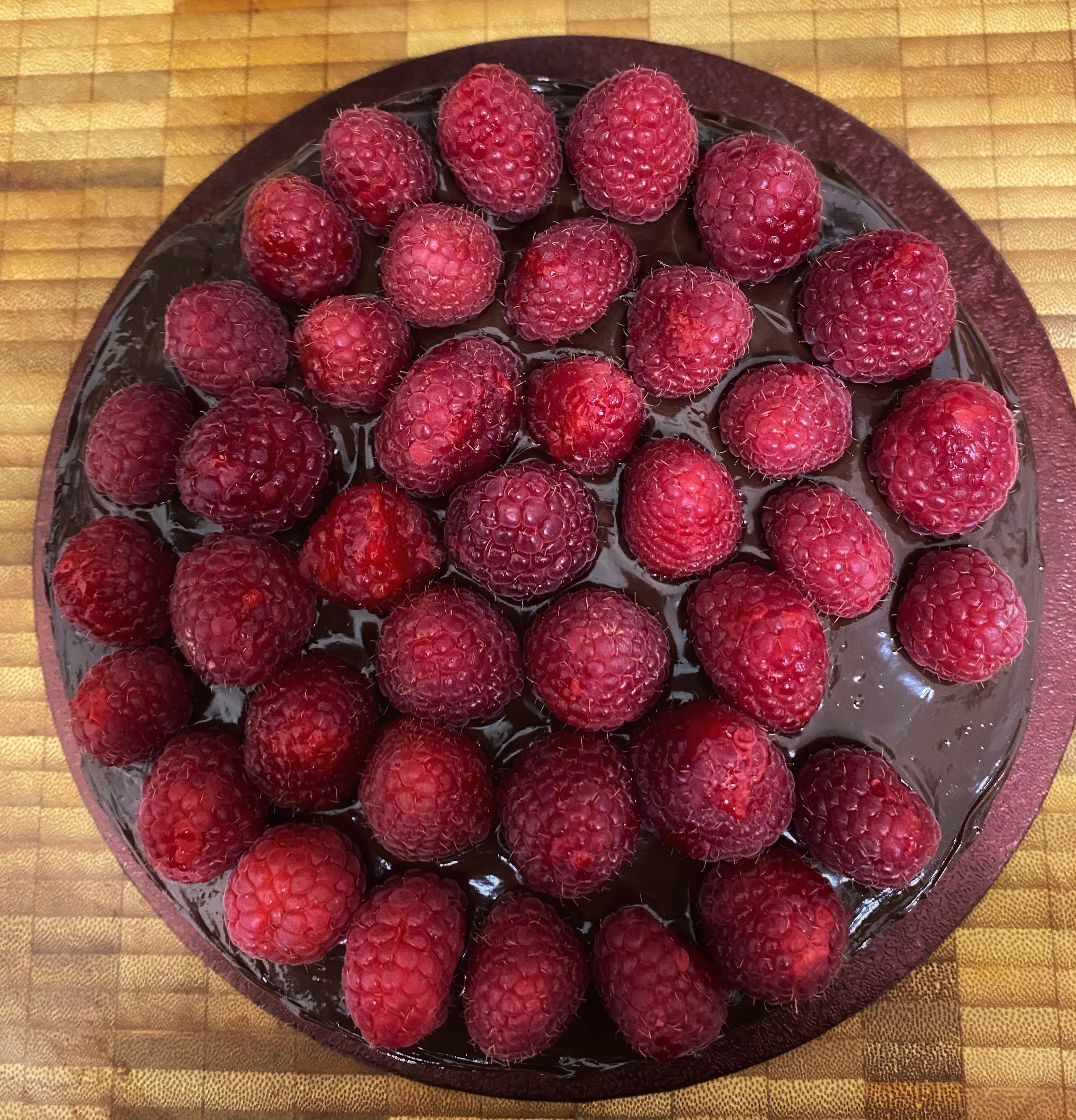 A top-down image of a slightly scruffy-looking chocolate cake covered in fresh raspberries